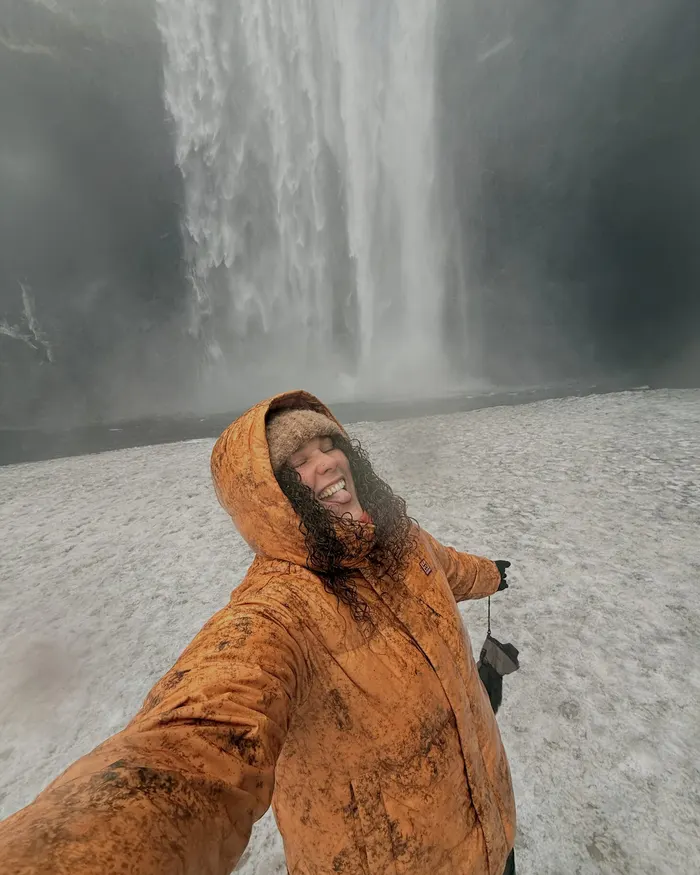 Anna grinning in a copper raincoat in front of a huge Icelandic waterfall, soaked through