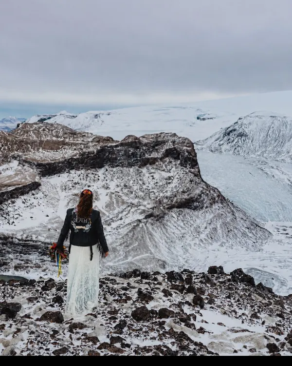 Anna in a lace wedding dress and painted leather jacket, standing above a glacier in Iceland